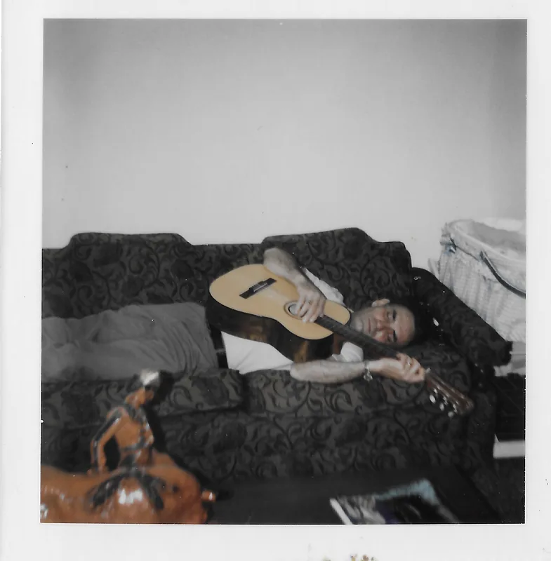 A man lying on a couch with an acoustic guitar resting on his chest