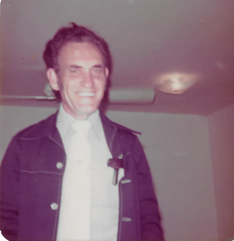 A smiling man in a dark jacket and white shirt, in a faded 1970s color photograph