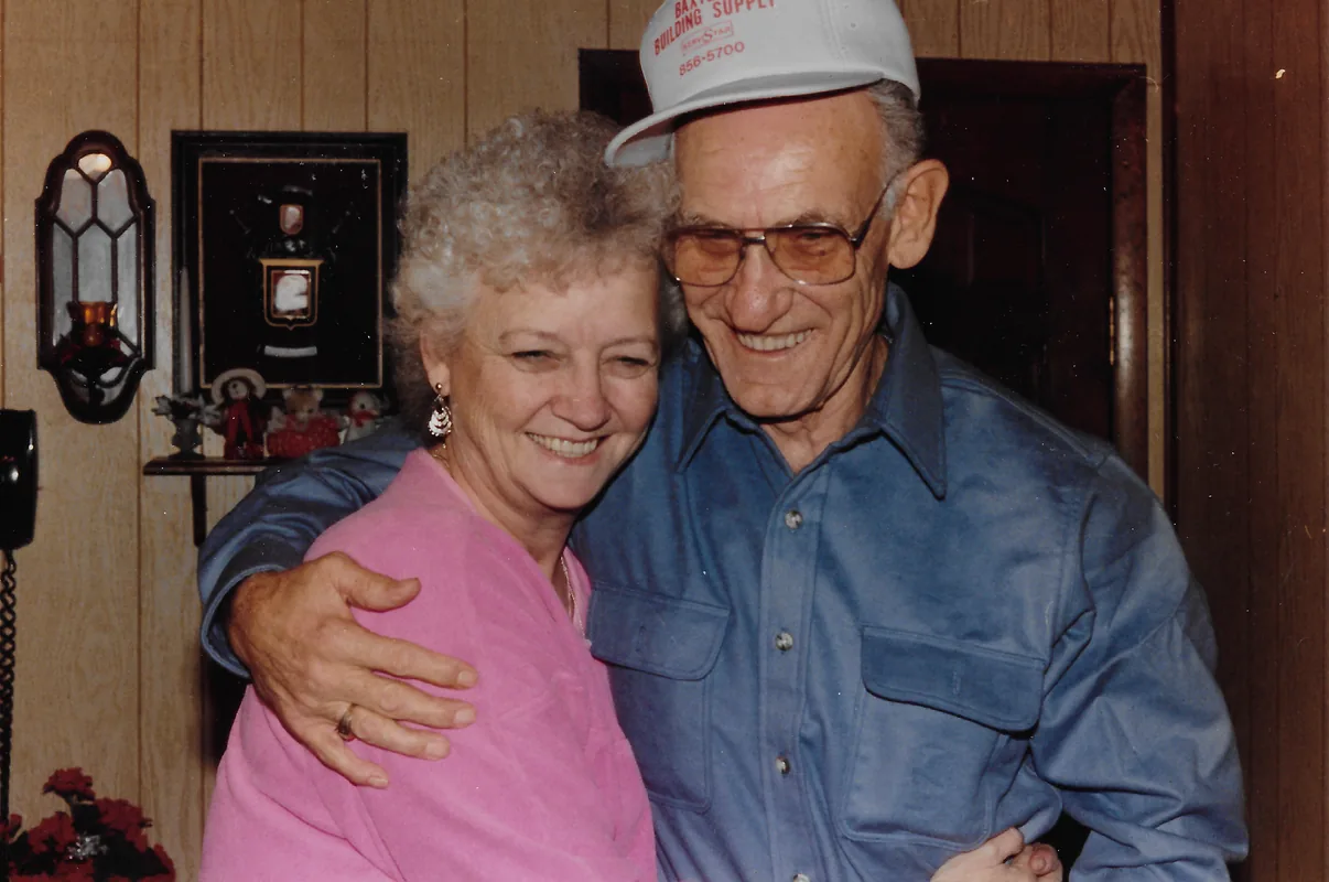 A smiling older woman in a pink top and a man in a white cap embrace